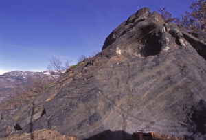 10.Le rocher noir de Chadel avec « marmite » d’érosion sous-glaciaire. Il s’agit d’une métabasite en faciès éclogite, avec omphacite et grenat.